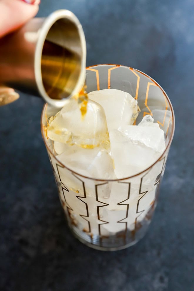 Pouring whiskey into a highball glass filled with ice