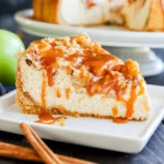 slice of caramel apple crumble cheesecake on plate with fresh apple and cinnamon sticks
