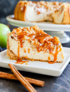 slice of caramel apple crumble cheesecake on plate with fresh apple and cinnamon sticks