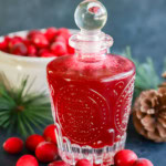 cranberry simple syrup in a jar with pinecone and frozen berries