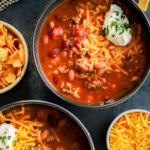 bowls of instant pot chili topped with cheese, sour cream, and parsley with fritos on the side