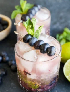 A cocktail glass with blueberry mojito garnished with fresh blueberries and mint leaves