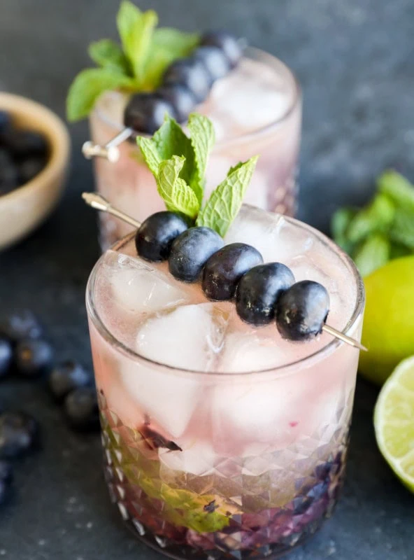 A cocktail glass with blueberry mojito garnished with fresh blueberries and mint leaves
