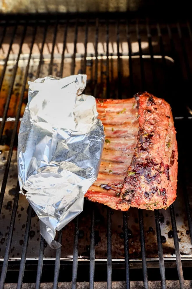 bbq rack of lamb on grill with aluminum foil wrapping the bones