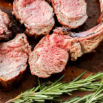 sliced rack of lamb on a cutting board with rosemary