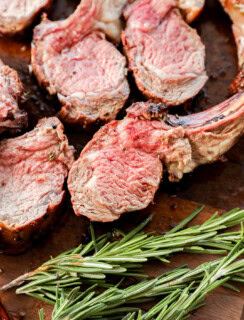 sliced rack of lamb on a cutting board with rosemary