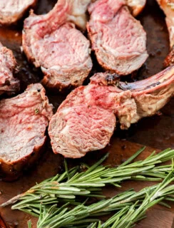 sliced rack of lamb on a cutting board with rosemary