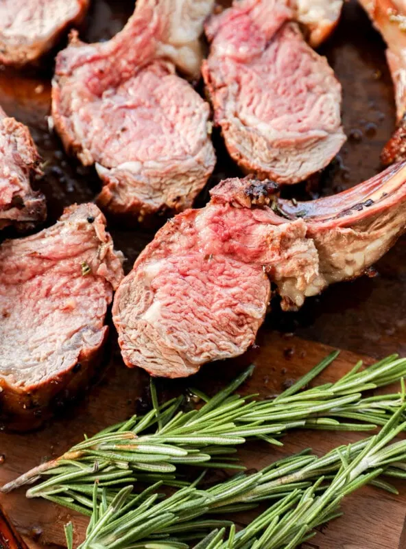 sliced rack of lamb on a cutting board with rosemary