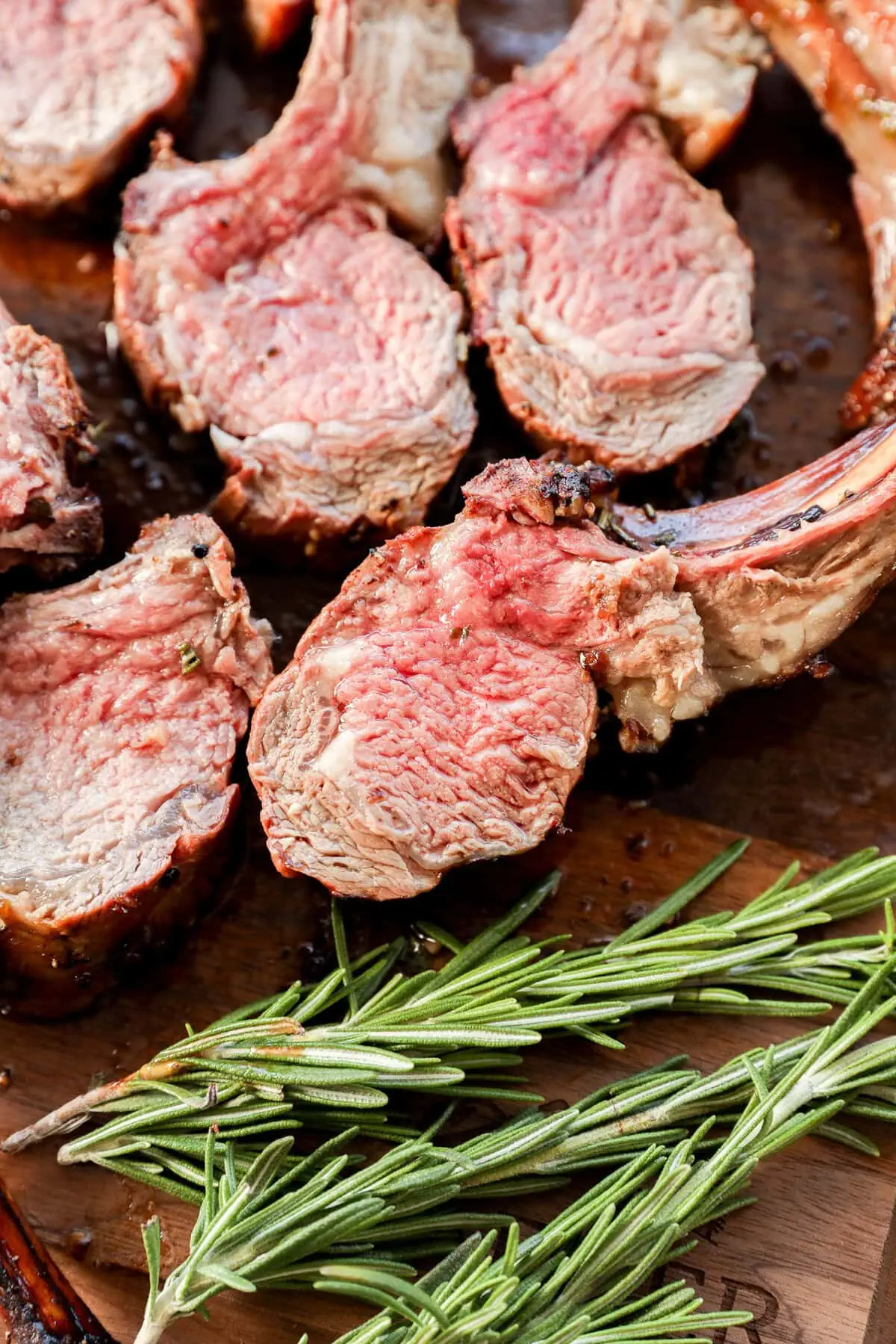 sliced rack of lamb on a cutting board with rosemary