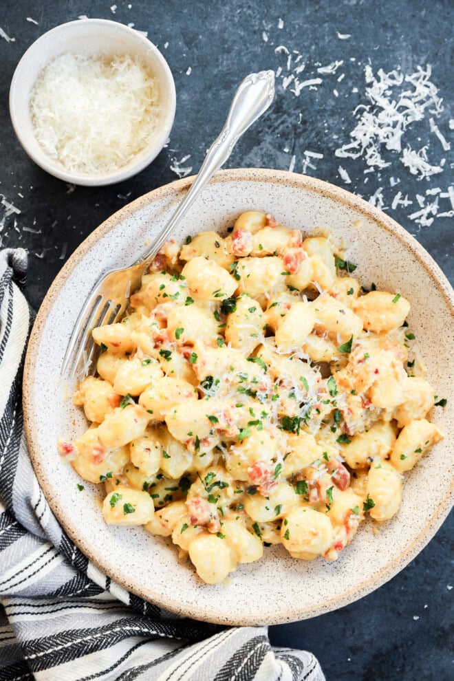 Bowl of gnocchi carbonara with cheese and fresh herbs and a fork