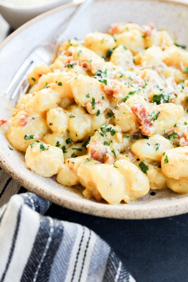 Easy Italian pasta dish in a bowl with cheese sauce and pancetta on linen and black