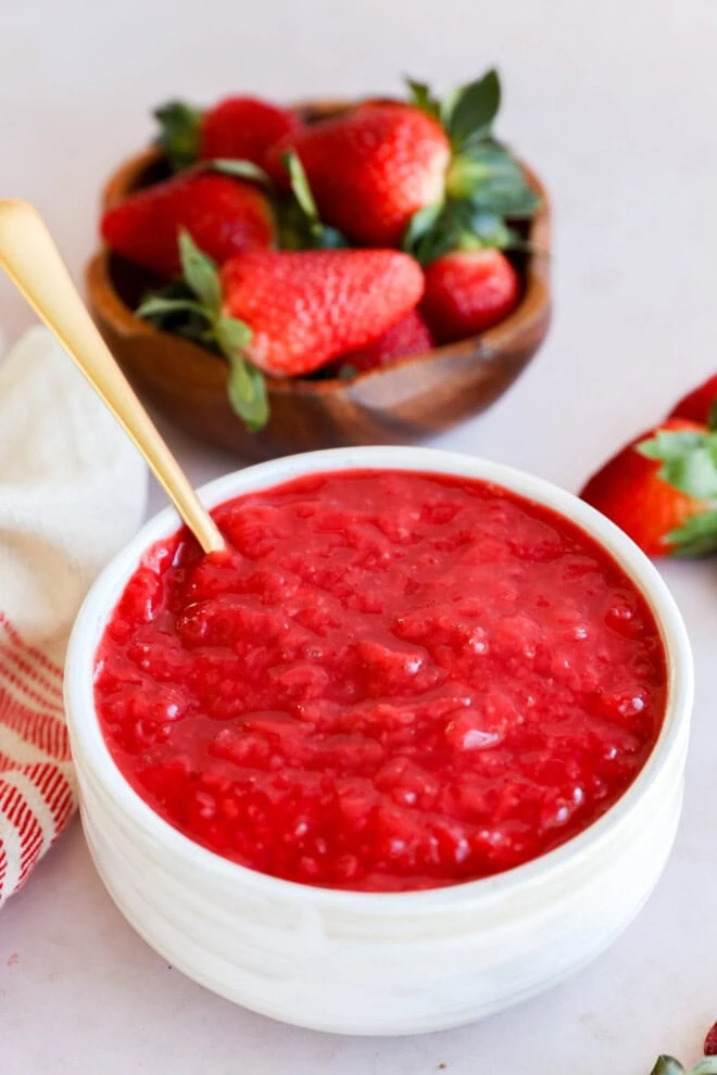 bowl of berry compote with spoon and bowl full of strawberries in the background