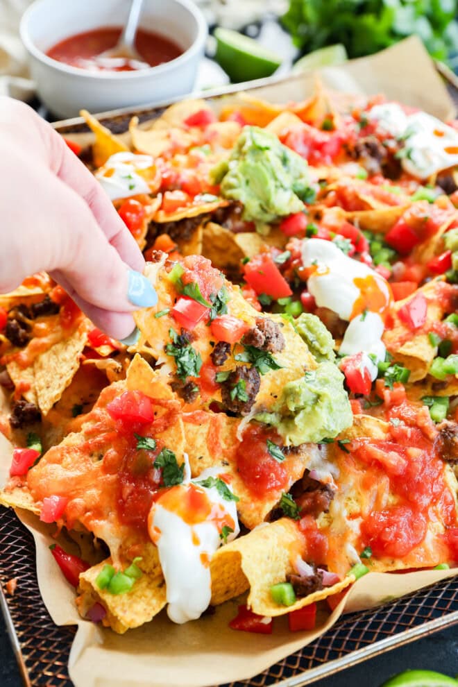 Air fryer nachos hand pulling it out of the tray
