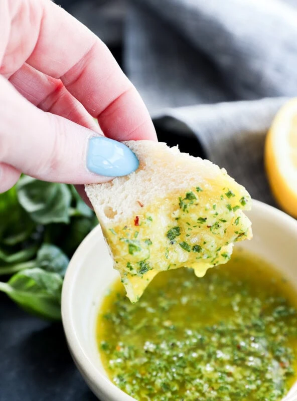 Hand holding a piece of bread dipping in a bowl of basil oil