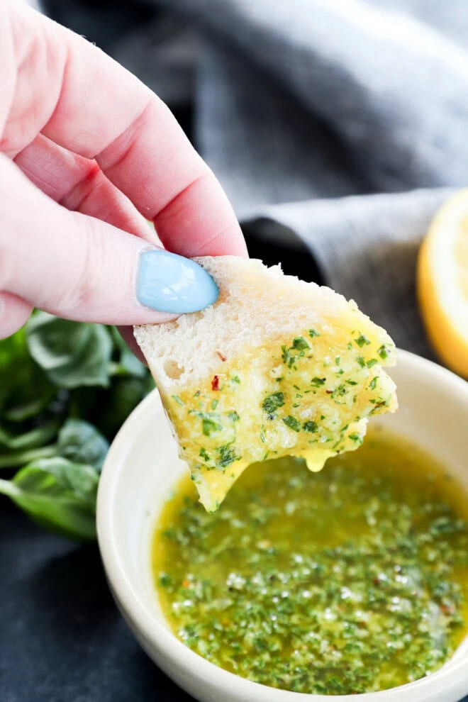 Hand holding a piece of bread dipping in a bowl of basil oil