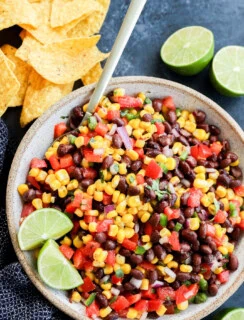 fresh and easy Black bean corn salsa dip in a bowl with a spoon and tortilla chips all around