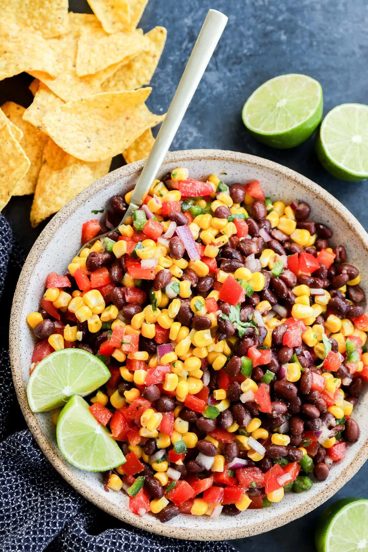 fresh and easy Black bean corn salsa dip in a bowl with a spoon and tortilla chips all around