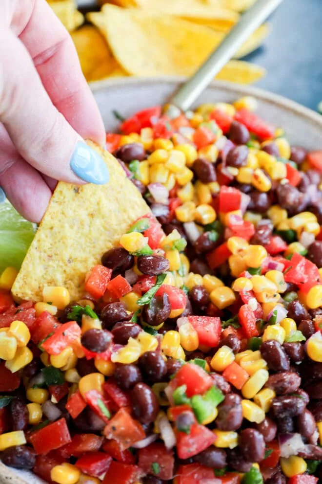 hand dipping a chip into a combination of fresh veggies in a bowl