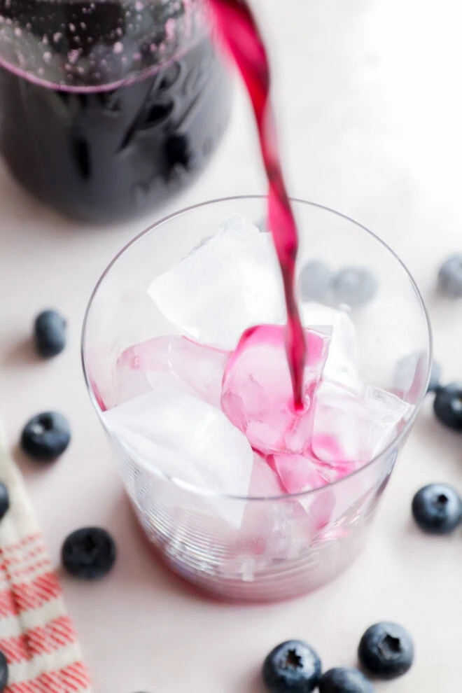 pouring blueberry simple syrup into a glass over ice