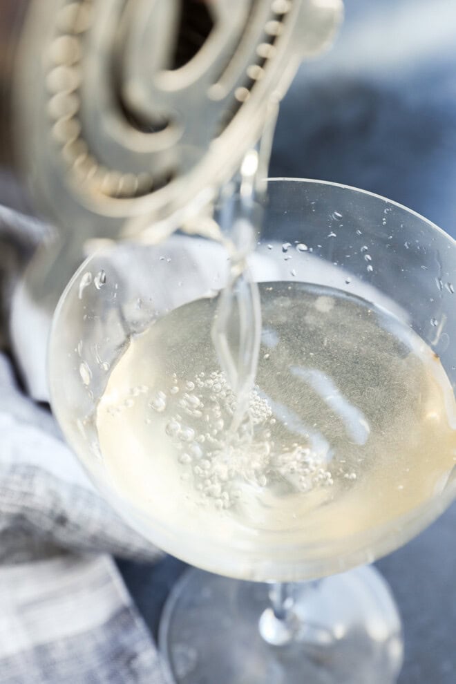 pouring a shaken dirty martini into a cocktail glass