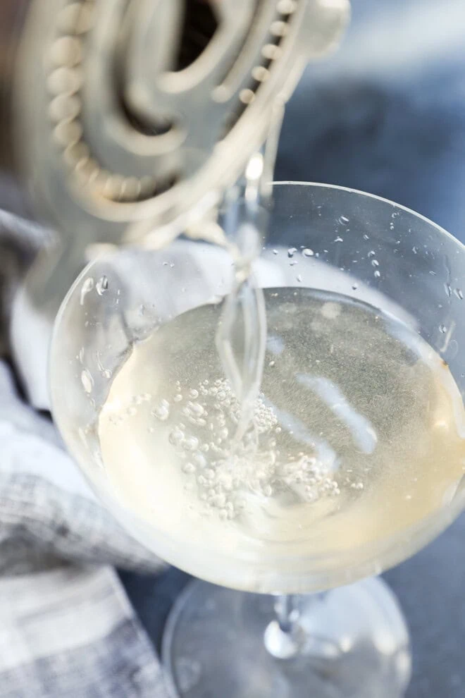pouring a shaken dirty martini into a cocktail glass