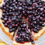 taking a slice out of lemon blueberry cheesecake on a cake stand