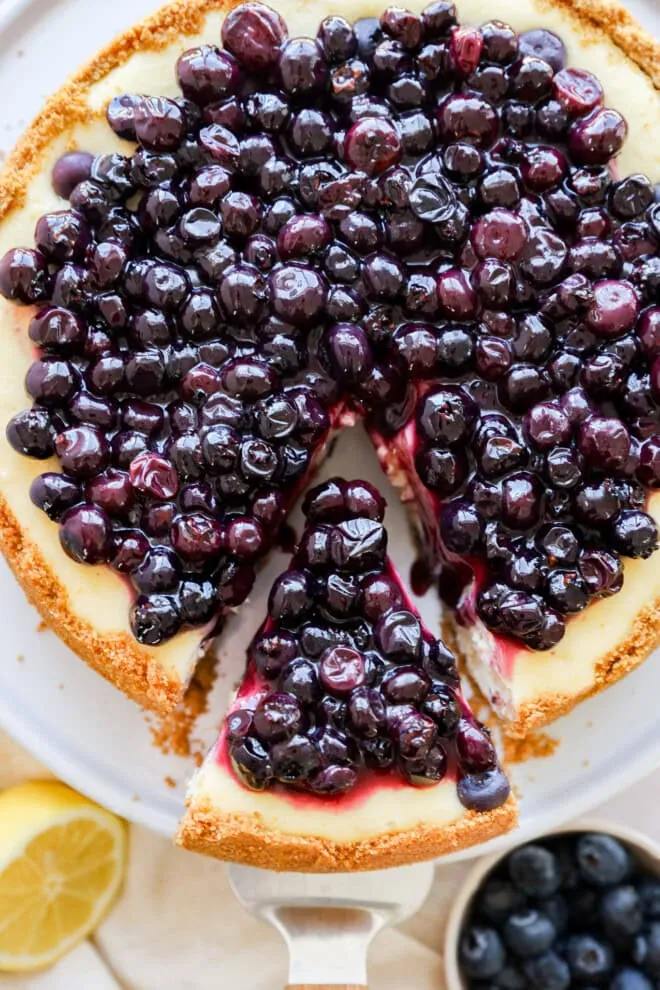taking a slice out of lemon blueberry cheesecake on a cake stand