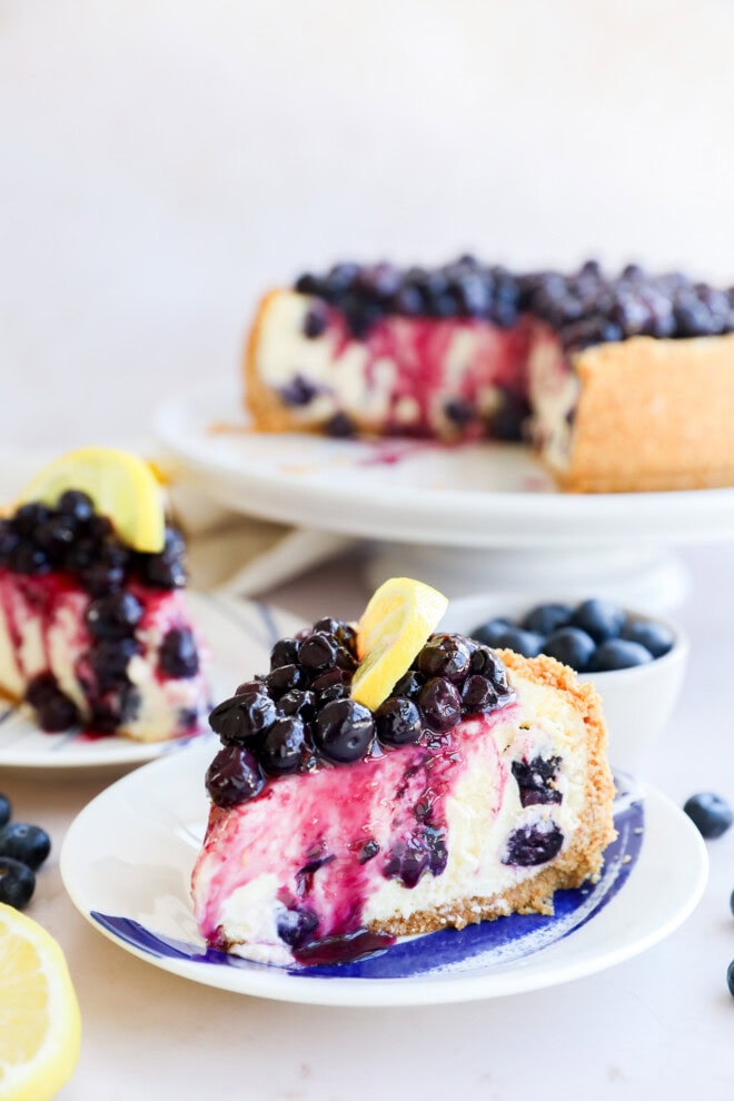 lemon blueberry cheesecake slices on plate with cake on cake stand