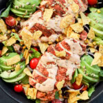 large bowl with healthy meal with lettuce, avocado, poultry, dressing, chips, seeds