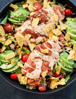 large bowl with healthy meal with lettuce, avocado, poultry, dressing, chips, seeds