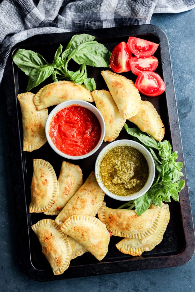 caprese empanadas on sheet pan with dipping sauces, fresh basil, and tomatoes