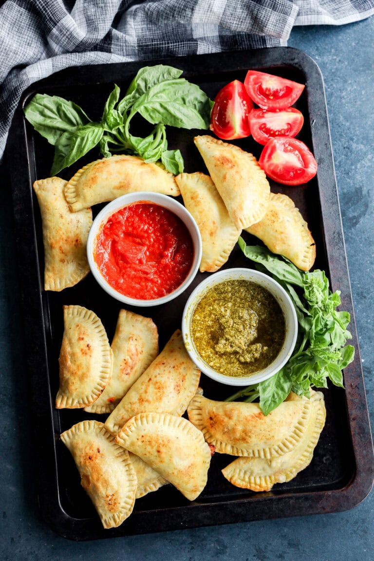 caprese empanadas on sheet pan with dipping sauces, fresh basil, and tomatoes
