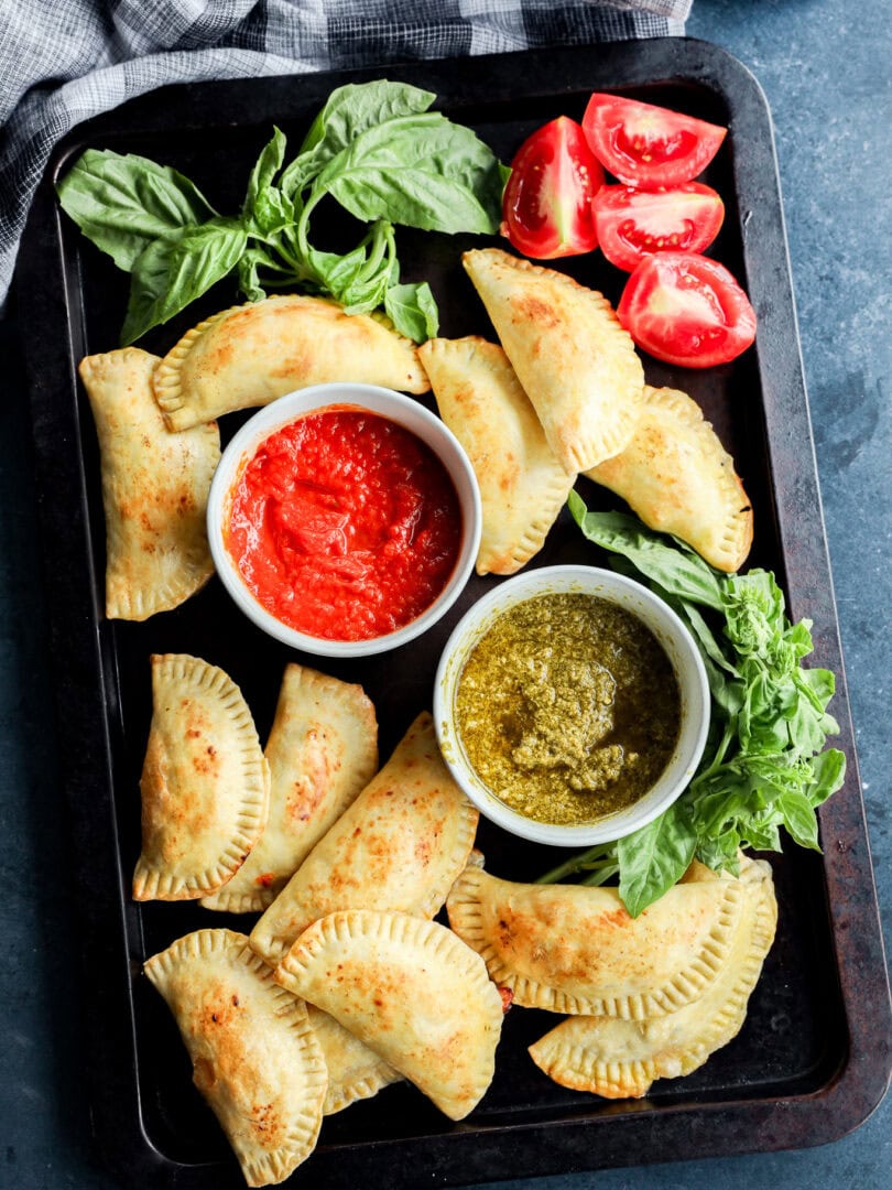caprese empanadas on sheet pan with dipping sauces, fresh basil, and tomatoes