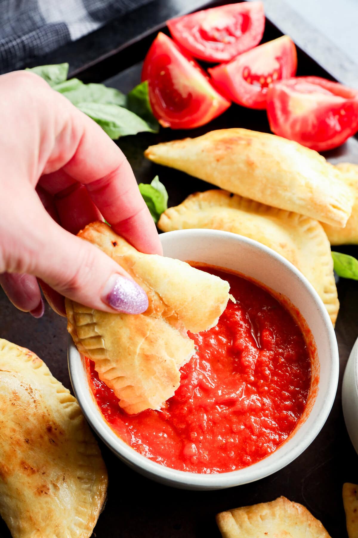 dipping a caprese empanada into a bowl of marinara sauce