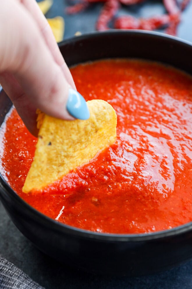 hand dipping a chip into a bowl of spicy red sauce