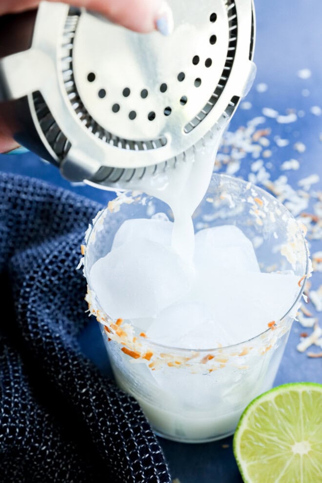 Pouring a Coconut margarita into a cocktail glass filled with ice