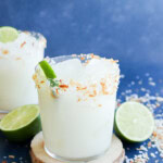 Easy tropical cocktail in glass on a coaster with fresh limes and coconut flakes