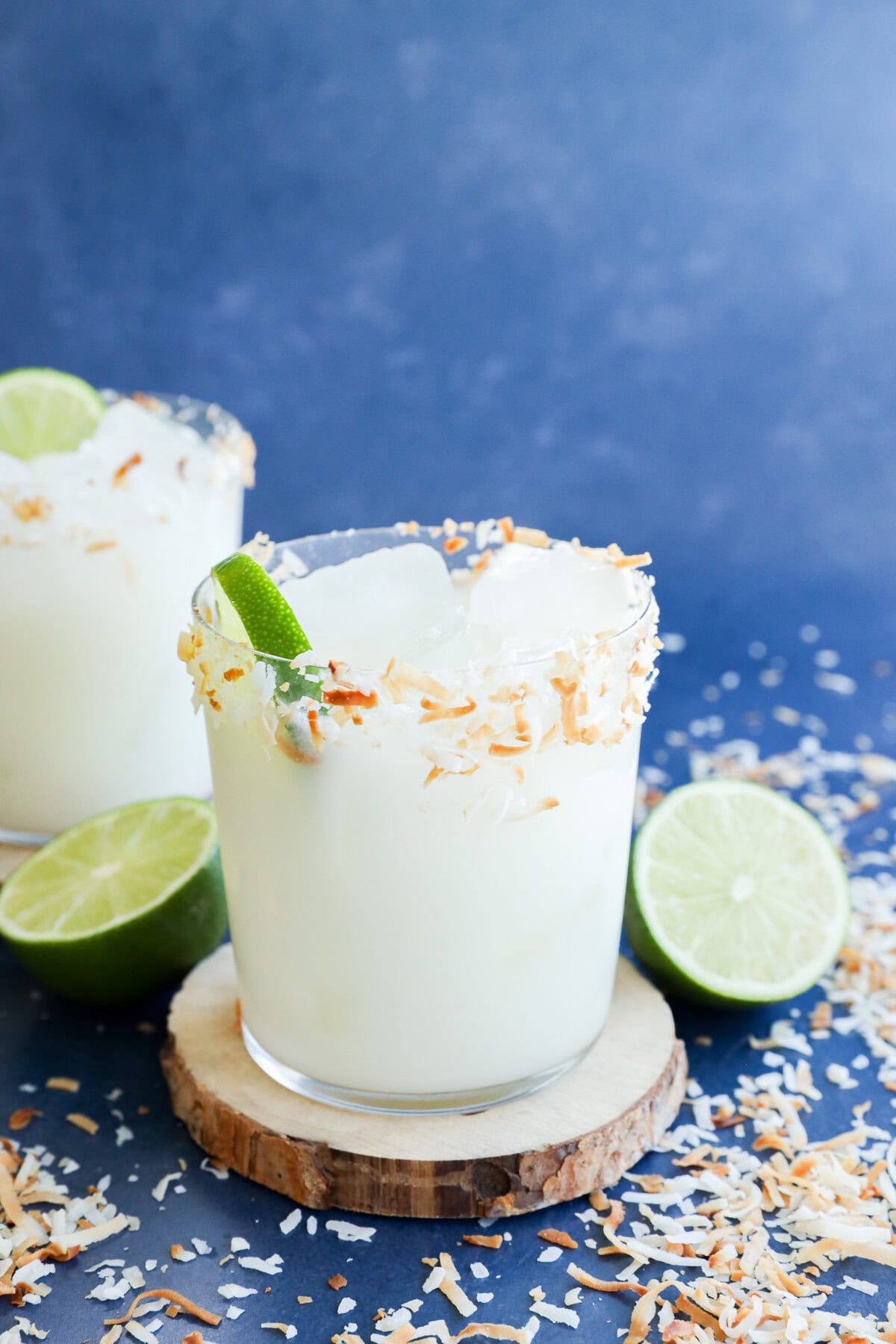 Easy tropical cocktail in glass on a coaster with fresh limes and coconut flakes