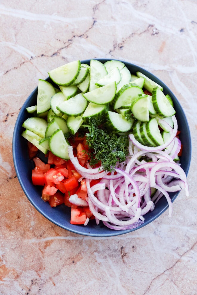 making Cucumber tomato salad in a blue bowl with marble counter