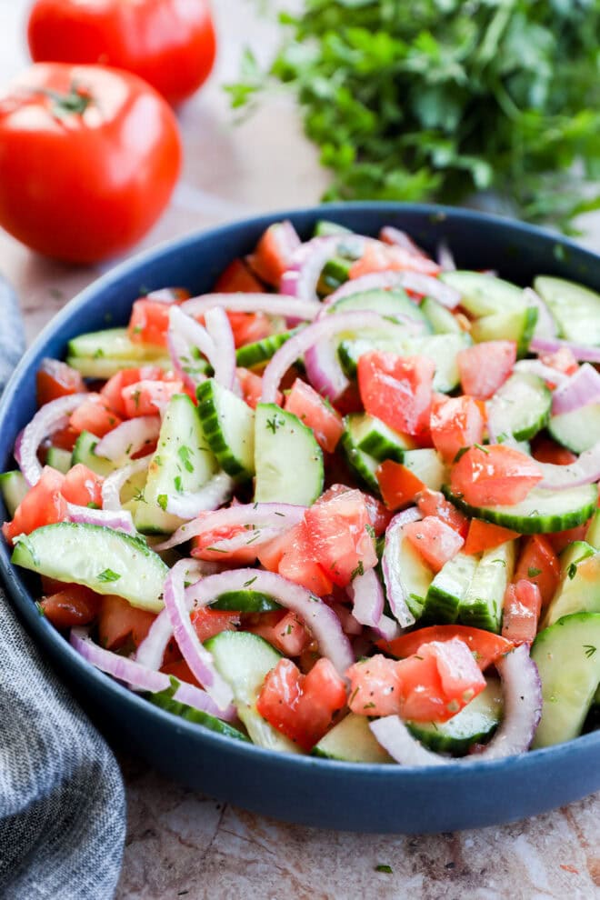 Fresh summer vegetables in a blue bowl with fresh veggies and herbs in the background