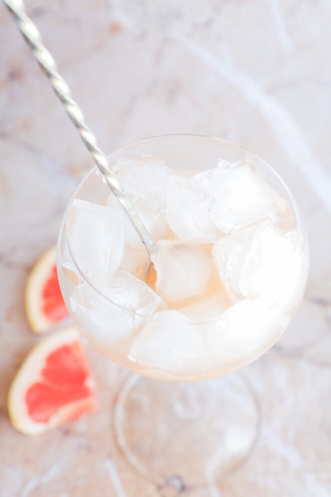 Wine, vodka, and grapefruit juice and elderflower liqueur in a glass with ice stirring with spoon