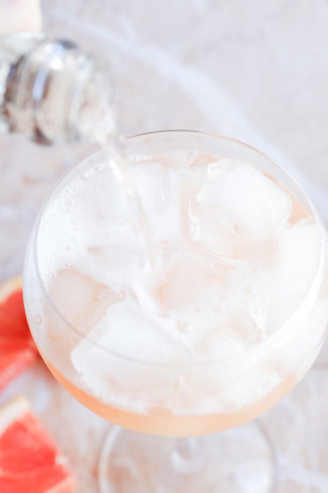 Pouring sparkling rośe into an elderflower cocktail on ice in a wine glass