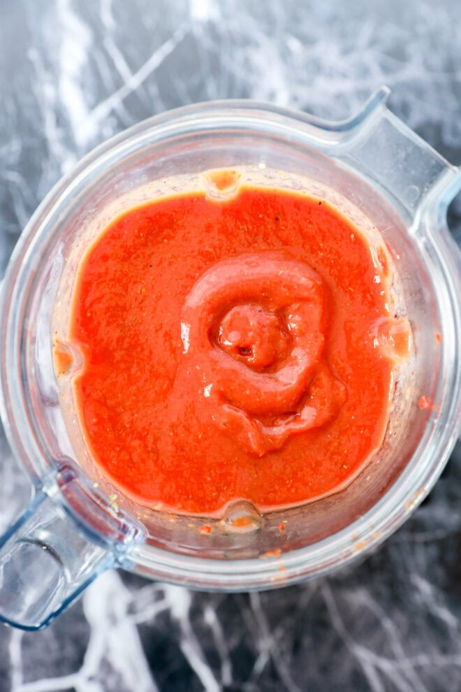 A blender filled with bright red Best Pizza Sauce, viewed from above, sits on a gray and white marble countertop.