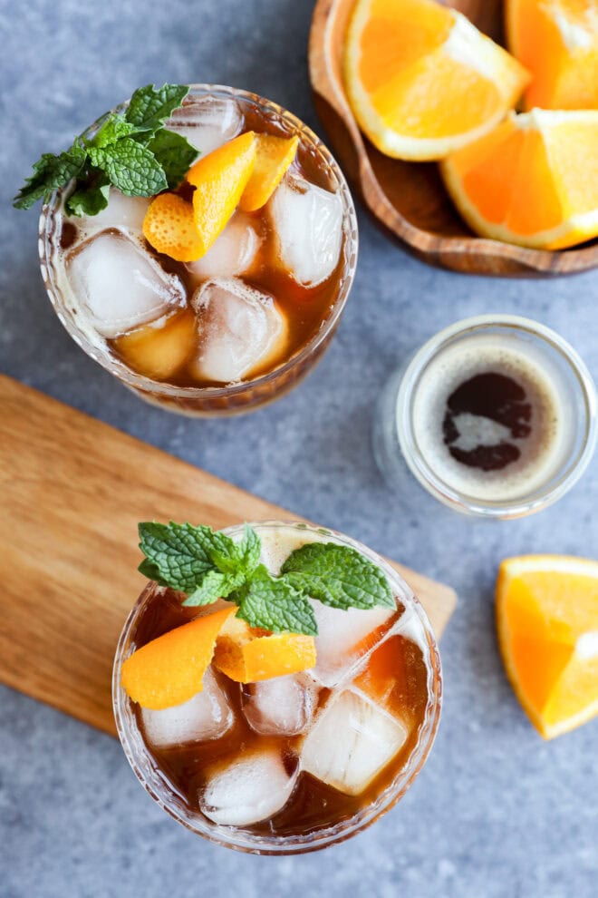 iced coffee drinks in glasses with mint and orange peel garnish