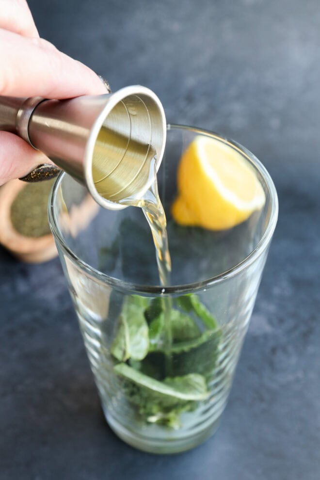 pouring green tea simple syrup into a shaker with mint leaves