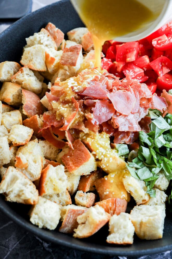 Drizzling dressing over Panzanella Toscana in serving bowl