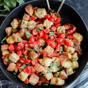 Panzanella Toscana in large black serving bowl with striped linen and fresh basil