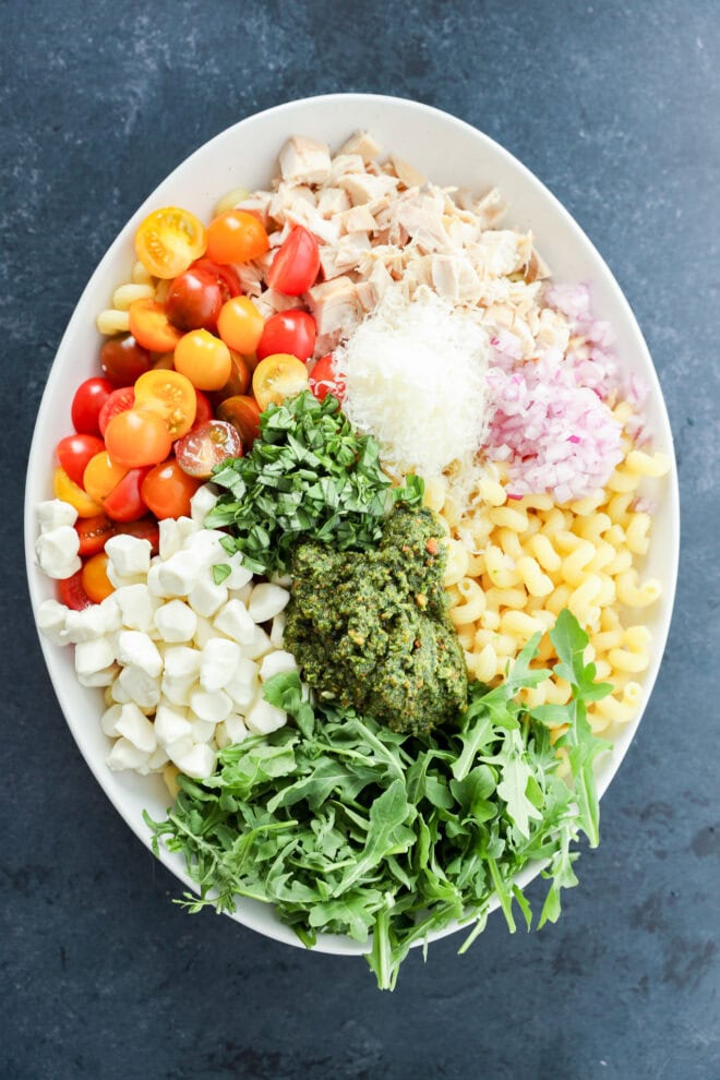 ingredients for pesto chicken pasta salad in a large serving bowl before mixing together
