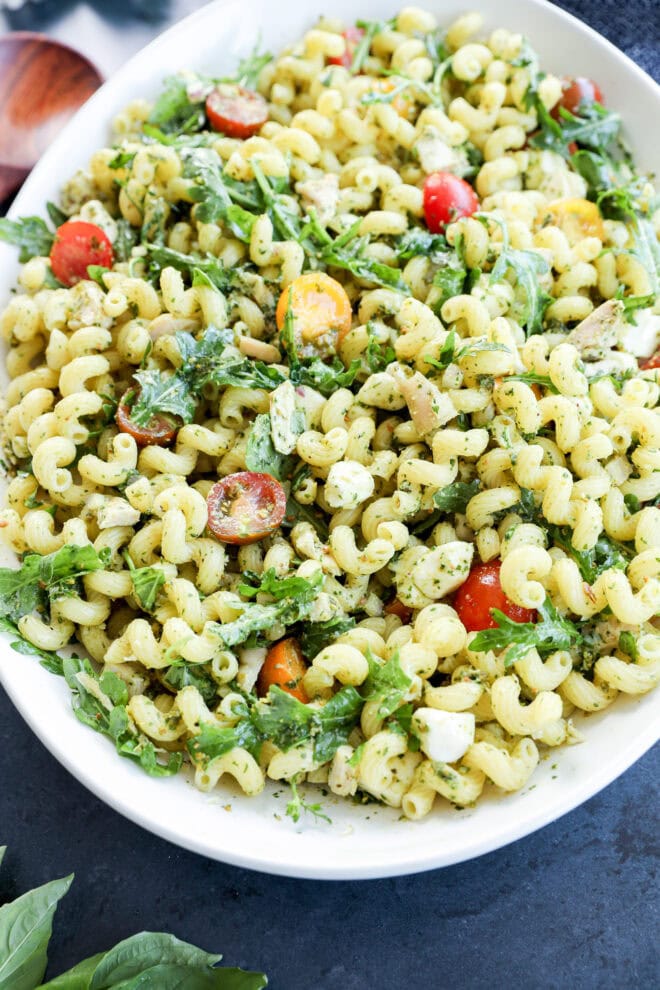 pesto chicken pasta salad in a large white serving bowl on black counter