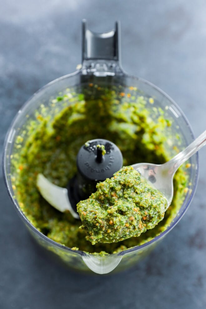 Spoon lifting out pistachio pesto from food processor after being made